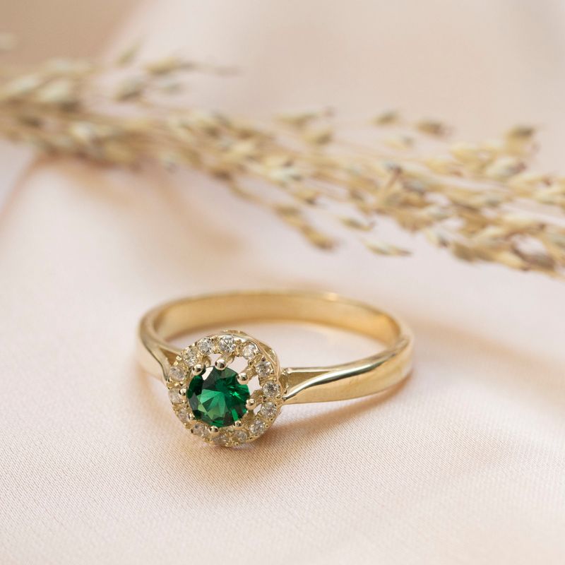 טבעת זהב צהוב עגולה עם זרקונים לבנים קטנים וזרקון ירוק במרכז